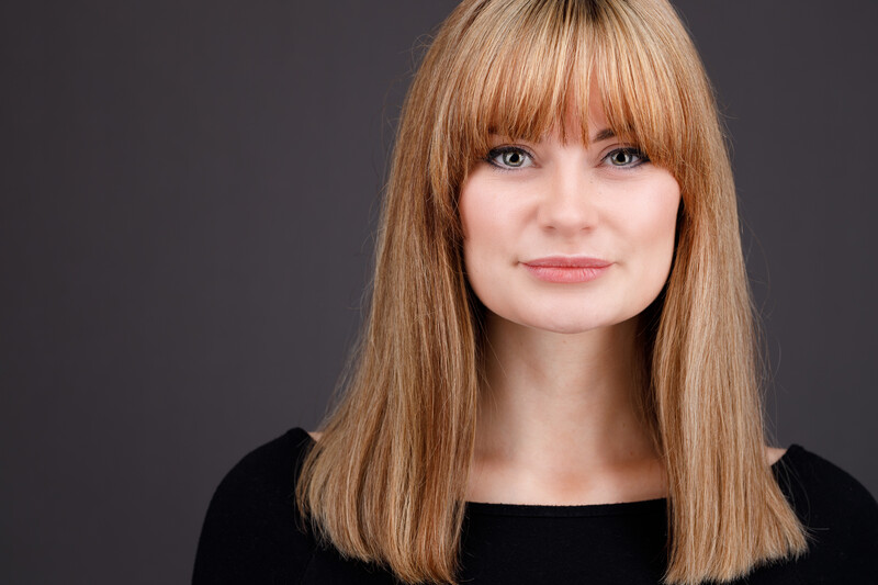 Woman with shoulder-length honey blonde hair and bangs against a neutral gray background.