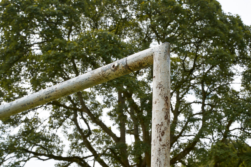 Weathered white painted metal pipe and post against dense green foliage background.