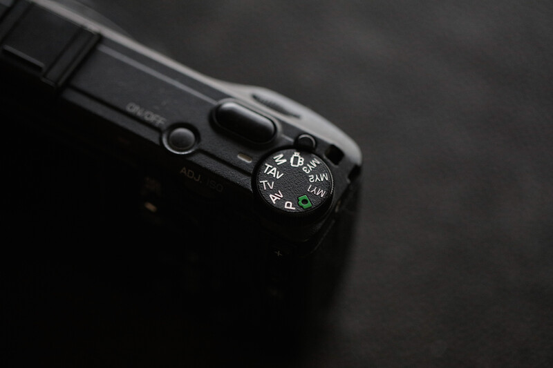 Close-up of a camera's mode dial showing aperture and shutter speed settings in black and white.