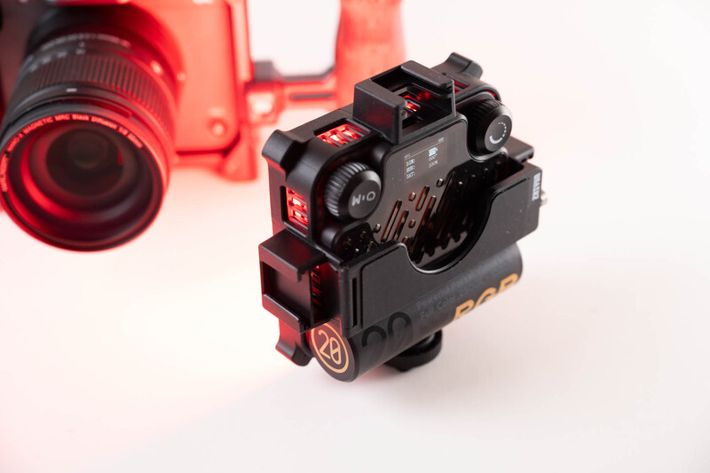 Black tactical rifle scope with illuminated red reticle mounted on Picatinny rail, photographed against blurred red-lit background.