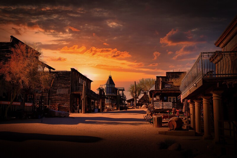 Western saloon street at golden hour with dramatic orange sky and long shadows across sandy ground.