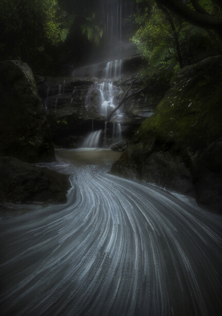Misty forest waterfall with silky flowing stream in foreground, long exposure photography.