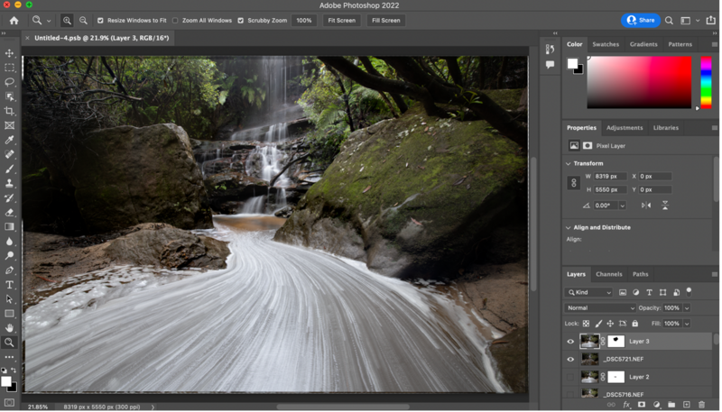Long exposure photograph of a flowing stream with smooth water effect cascading over moss-covered rocks and boulders.
