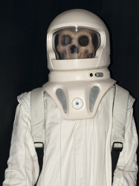Skeleton wearing a white spacesuit and helmet against a black background.