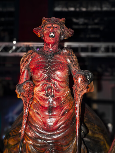 Anatomical sculpture with detailed musculature rendered in deep red and orange tones under dramatic lighting.