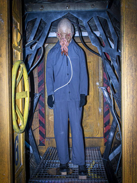 Man in blue suit standing in an elevator with stylized blue lightning bolt graphics on the walls.