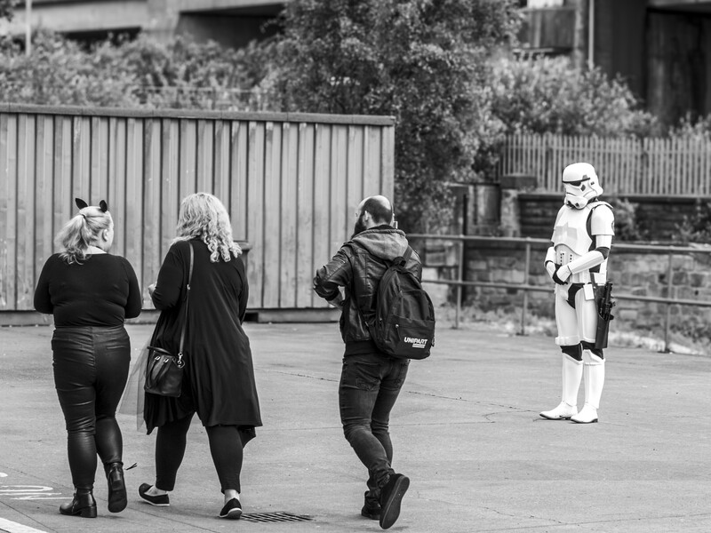 Three people walking away from a person in a stormtrooper costume standing in an urban courtyard.