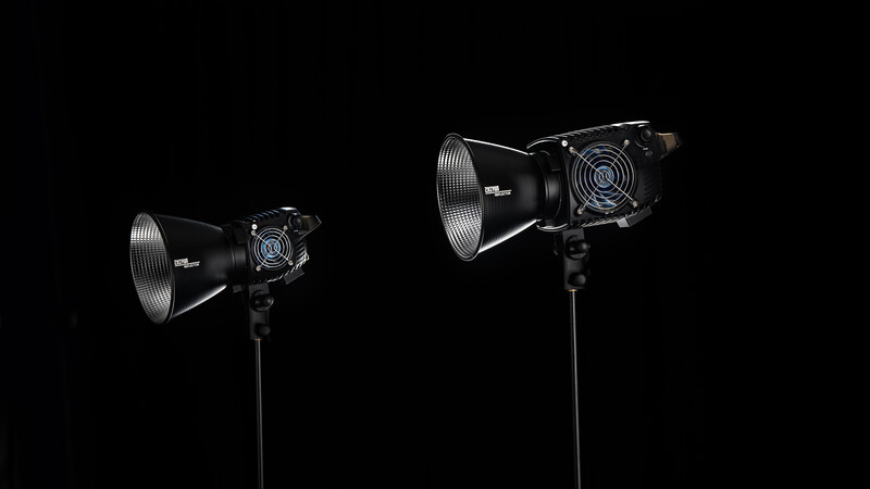 Two studio lighting fixtures with reflector dishes and cooling fans mounted on stands against a black background.