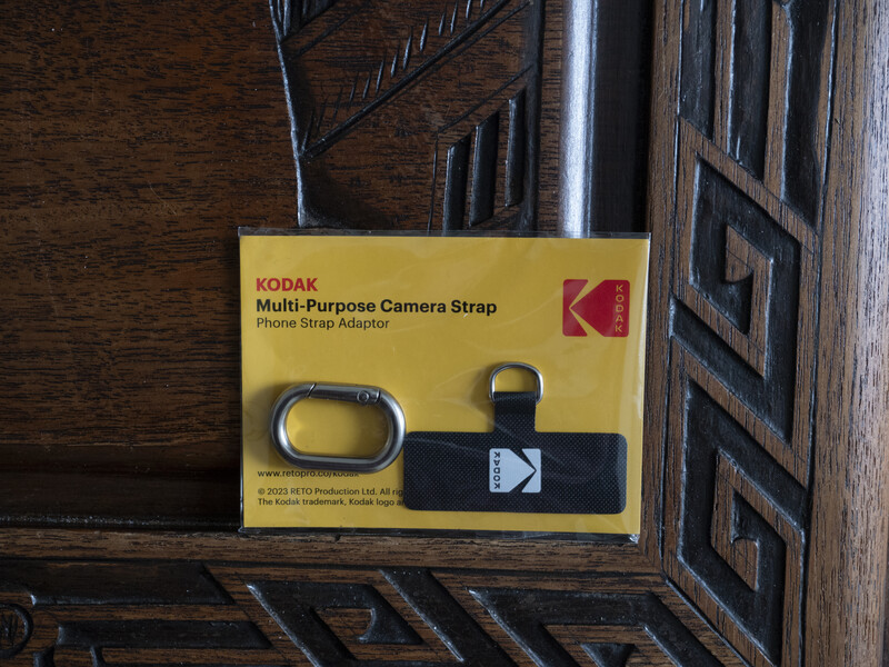 Kodak Multi-Purpose Camera Strap product packaging with phone adapter components on wooden surface.