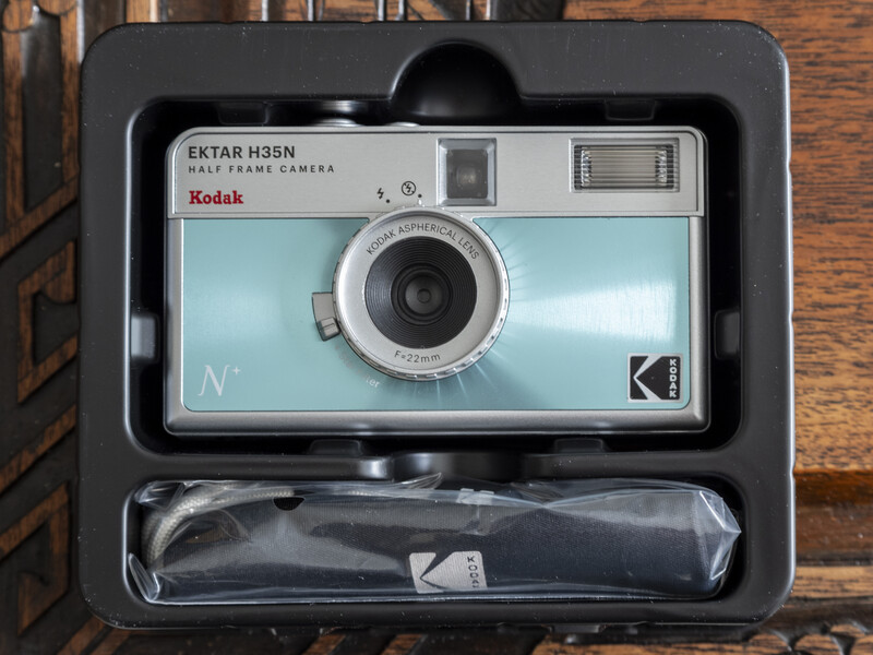 Kodak Ektar H35N half-frame camera in light blue with original packaging and strap on wooden surface.