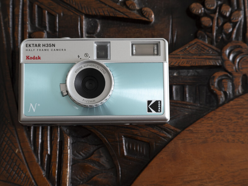 Kodak Ektar H 35N instant film camera with light blue body positioned on carved wooden surface.