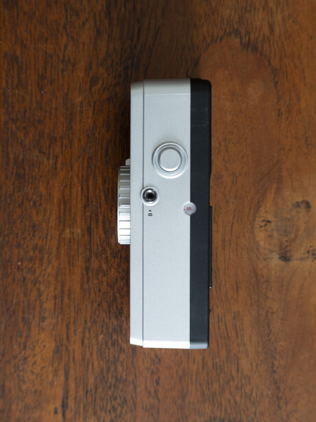 White and black rectangular device mounted on a wood-grain surface with a circular button and small camera lens visible.