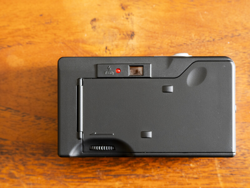 Top view of a compact film camera with dark gray body and mechanical shutter button on wooden surface.
