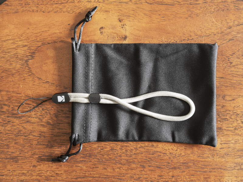 Black fabric pouch with drawstring closure and white cord loop on wooden surface.