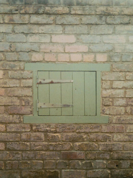 Weathered brick wall with pale green painted wooden door frame and planks.
