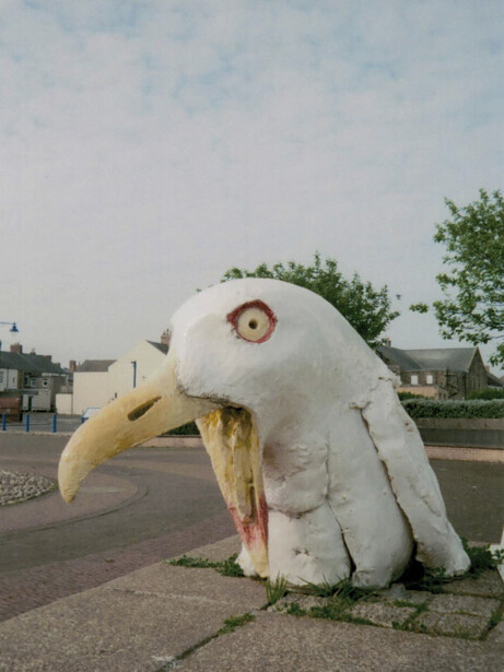 Large white sculptural eagle head with open beak displayed in a public plaza.