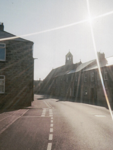 Stone street leading toward a church with a prominent tower under bright sunlight with lens flare.