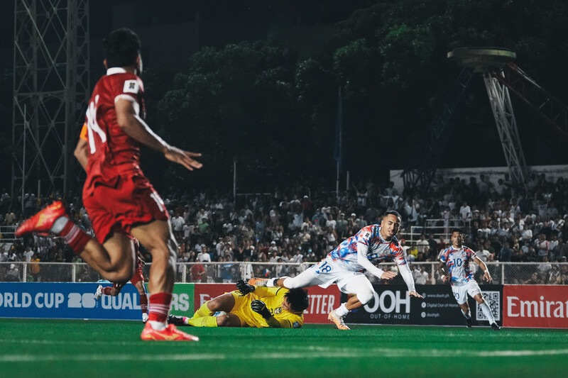 Rugby player in white jersey diving to score a try against a red-uniformed defender during a night match.