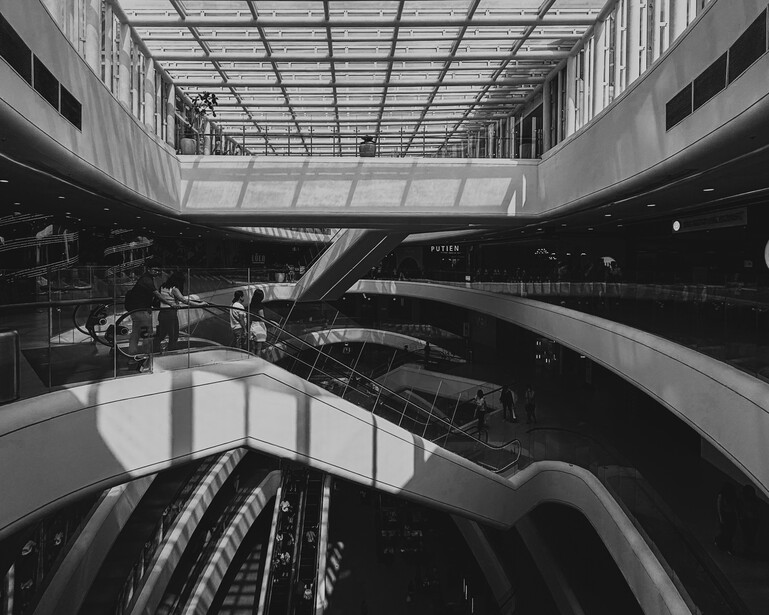 Black and white photograph of a modern multi-level interior with escalators and geometric architecture.