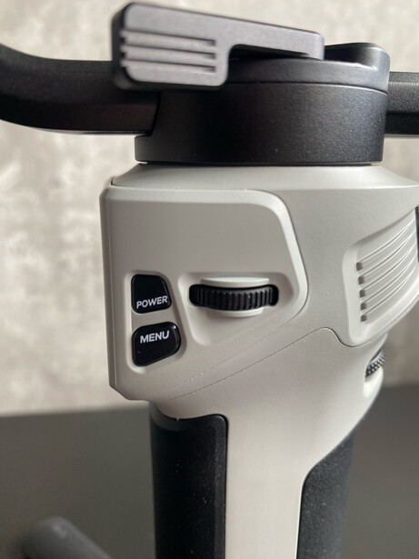 Close-up of a gimbal head's control panel showing power and menu buttons against a neutral background.