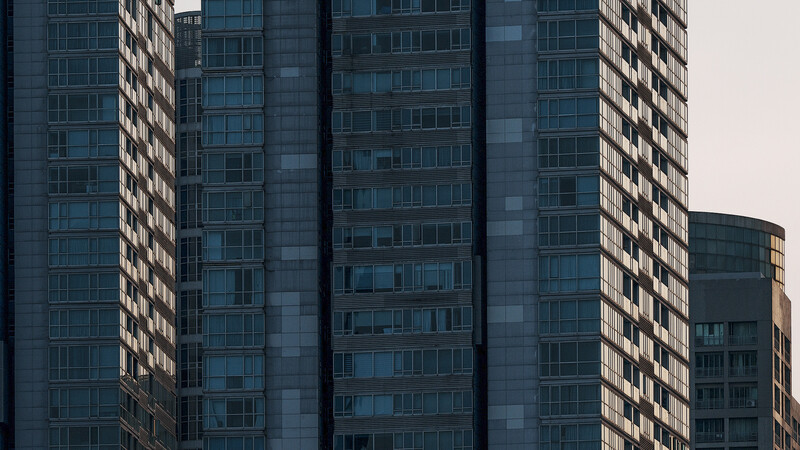 Tall residential high-rise buildings with gridded facade and repetitive window pattern against overcast sky.