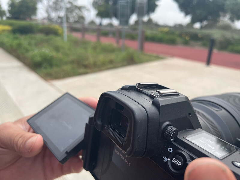 Photographer demonstrating articulating LCD screen on mirrorless camera outdoors.