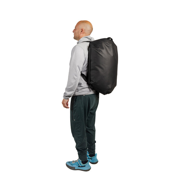 Man wearing black backpack standing in profile against white background.