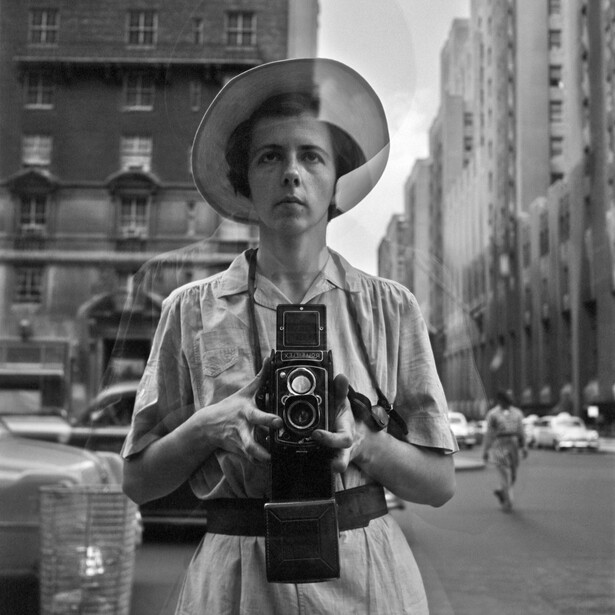 Street photographer holding a twin-lens reflex camera on an urban street.