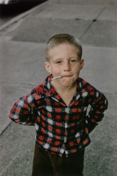 Young boy in red plaid jacket posing outdoors on concrete surface.