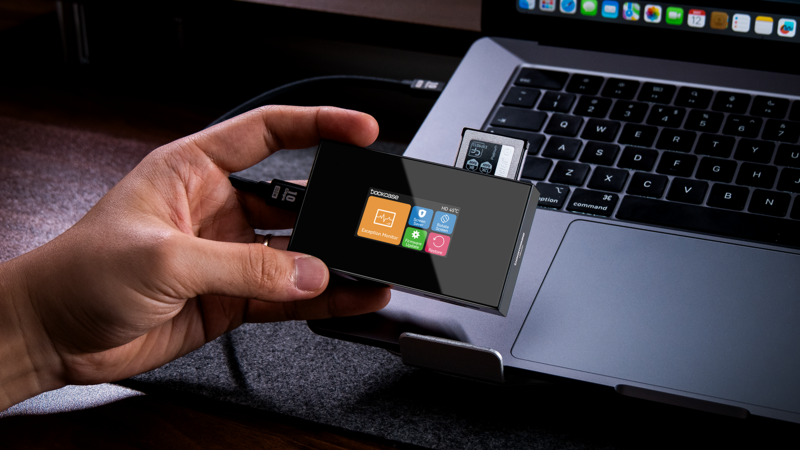 Hand holding a small portable external hard drive next to a laptop keyboard.