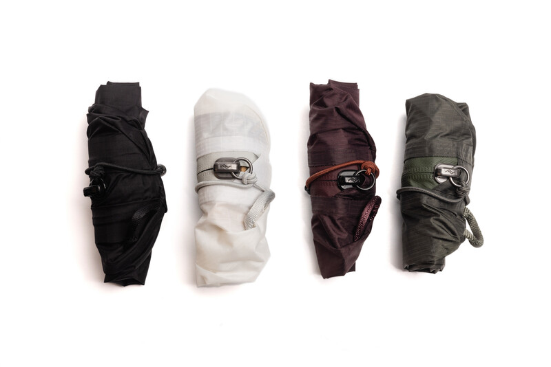 Four rolled fabric pieces in black, white, burgundy, and olive green, each secured with metal buckles.