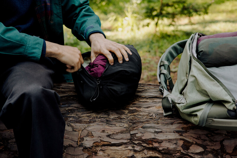 Hiker examining contents of black backpack while seated on a log outdoors.