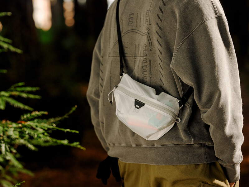 Person wearing khaki jacket and olive pants with white crossbody bag slung across shoulder at night.
