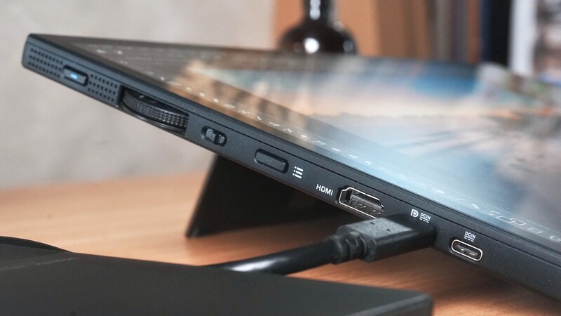 Laptop displaying landscape photograph with visible ports and cable connections on wooden desk.