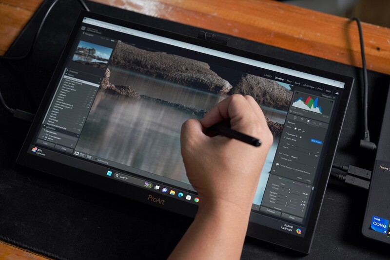 Photographer's hand using a stylus on a tablet displaying photo editing software with landscape image.