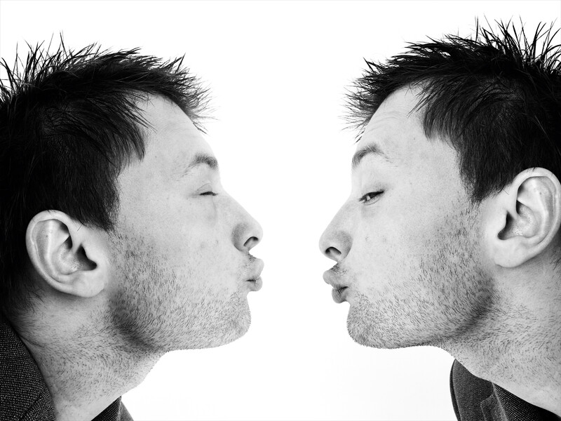 Two men face each other in profile against a white background, shot in black and white.
