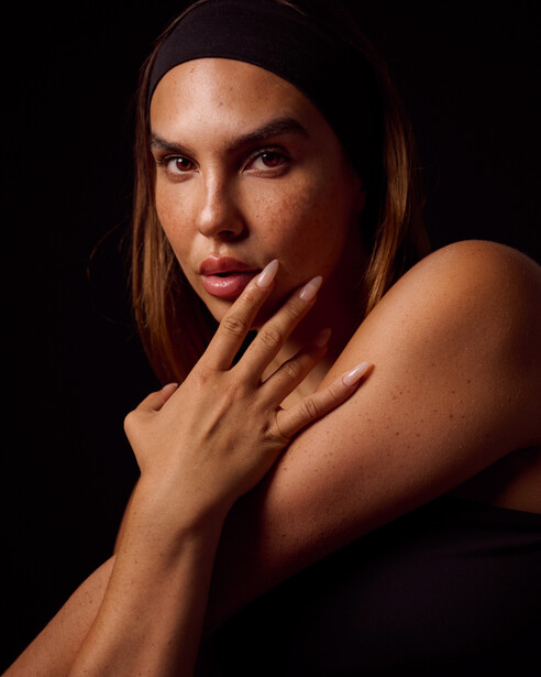 Woman with hand near face against dark background in studio lighting.
