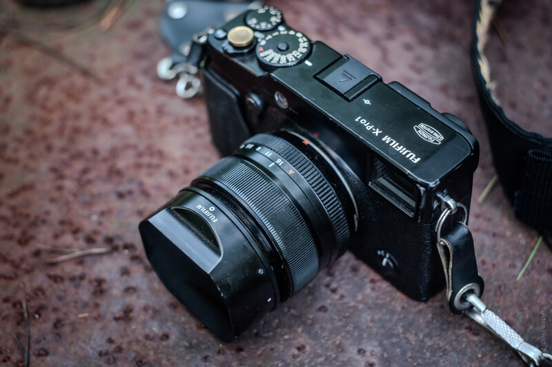 Black rangefinder camera with attached zoom lens on textured ground surface.
