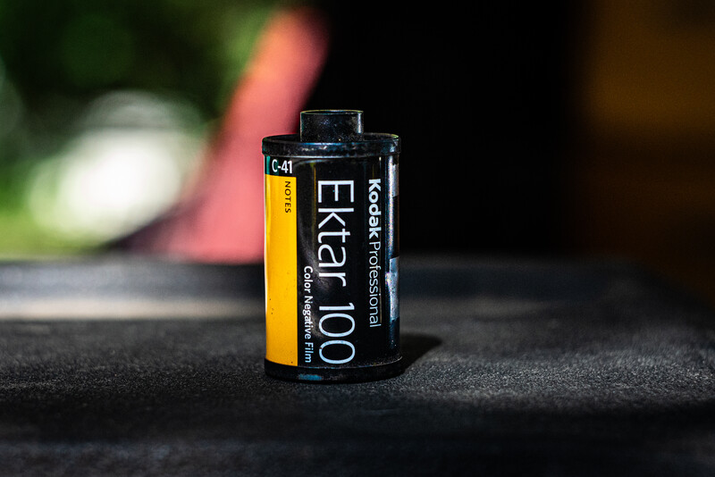 Kodak Ektachrome 100 color slide film canister on dark surface with blurred background.