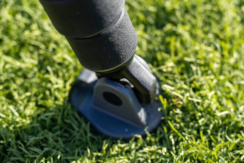 Hand holding a blue device pressed against green grass in bright sunlight.