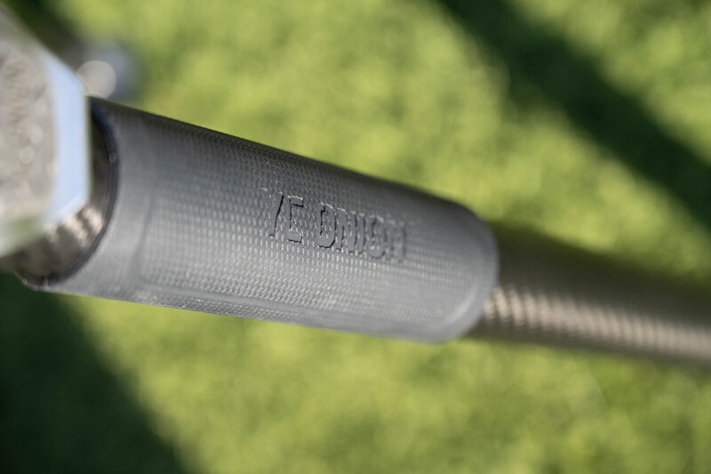 Close-up of a threaded metal connector or adapter with embossed text, photographed outdoors against blurred green foliage.