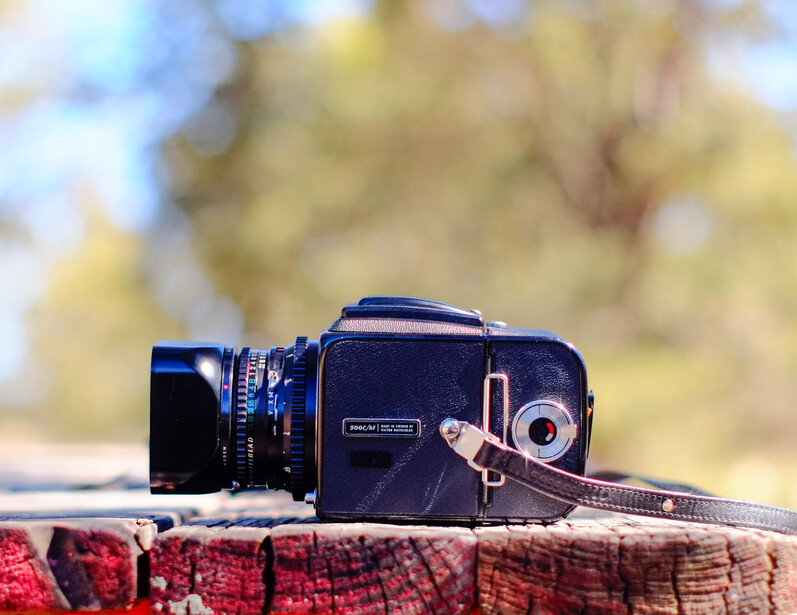 A vintage medium format film camera with attached lens and neck strap resting on a colorful woven fabric outdoors.