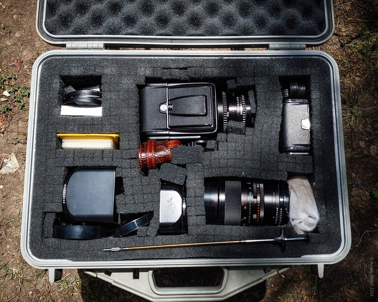 Open camera equipment case with organized foam insert holding lenses, camera body, flash, and accessories.