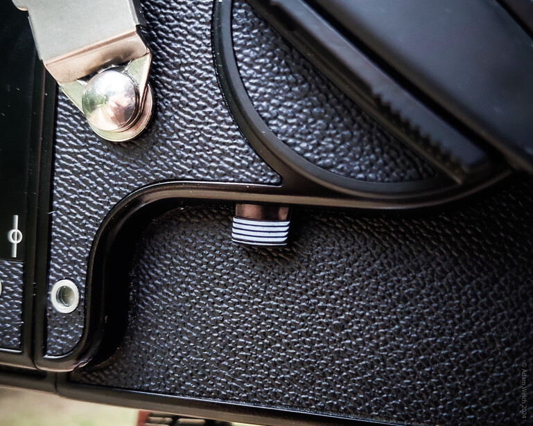 Close-up detail of vintage camera body showing textured leather covering, chrome accessories, and mechanical components.