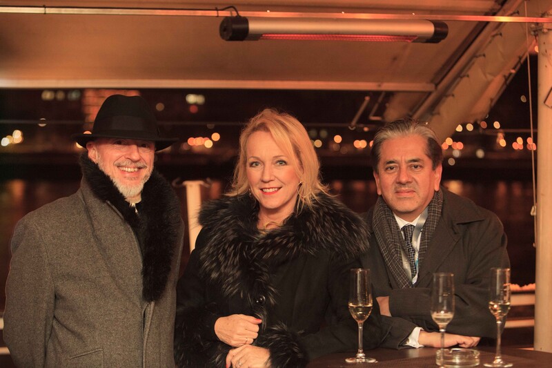 Three people posing together at an indoor event with warm ambient lighting and bokeh in the background.