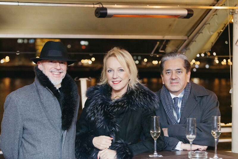 Three people posing together at an indoor evening event with warm ambient lighting in the background.