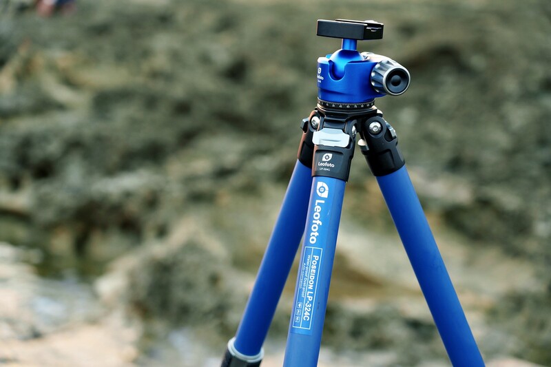 Blue tripod with ball head and panoramic mounting plate against blurred rocky background.