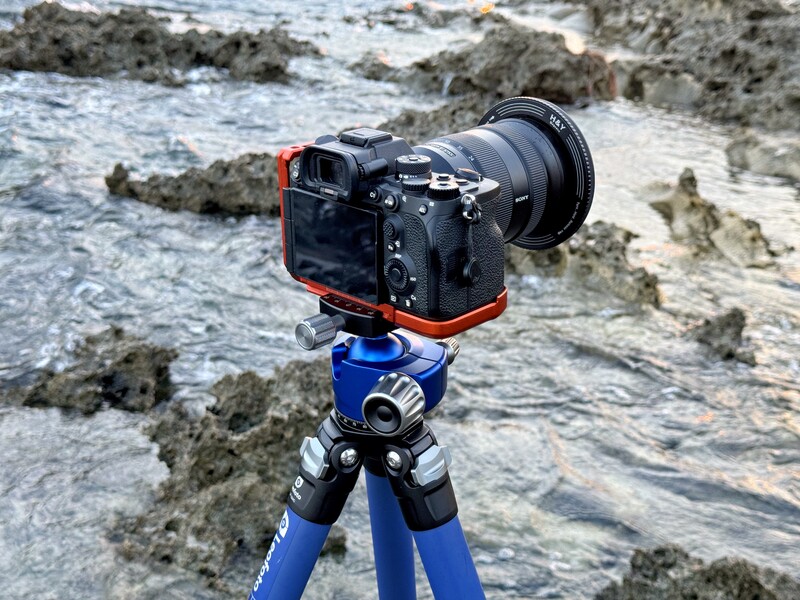 Professional camera mounted on blue tripod overlooking rocky coastal shoreline.