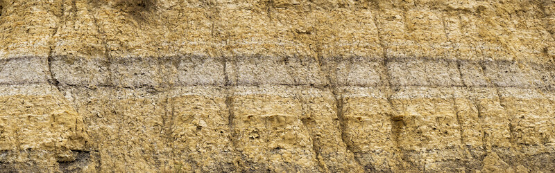 Close-up of layered stone wall with tan and gray brick courses showing texture and mortar joints.