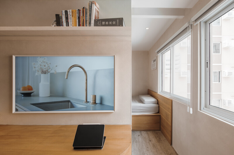 Modern apartment interior with framed kitchen sink photograph on beige wall above wooden desk with laptop.